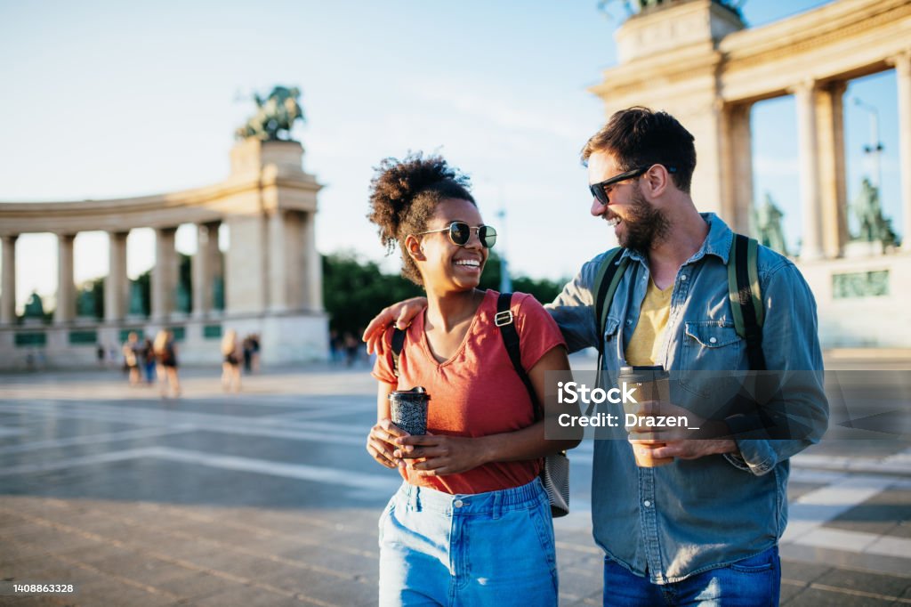 Beautiful young multiracial couple enjoying city break, holding coffee cups and wearing backpacks Couple travel throughout Europe Budapest Stock Photo