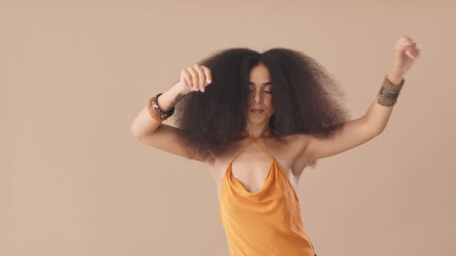 Beautiful hispanic young woman with an afro dancing in the studio. Beautiful young mixed race woman with an afro feeling confident and dancing with her arms raised