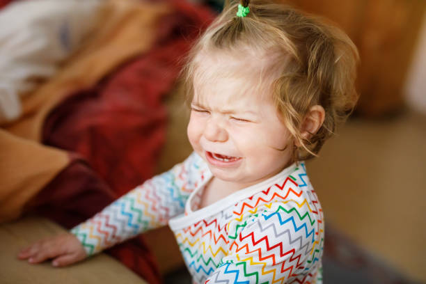 Cute upset unhappy toddler girl crying. Angry emotional child shouting. Portrait of kid with tears indoors stock photo