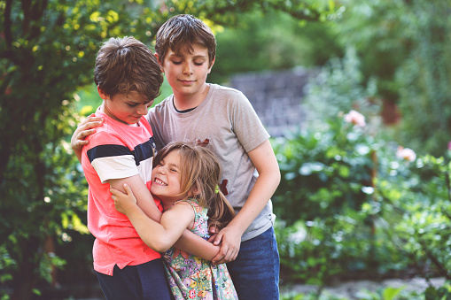 Portrait of three siblings children. Two kids brothers boys and little cute toddler sister girl having fun together in domestic garden. Happy healthy family playing, walking, active leisure on nature.