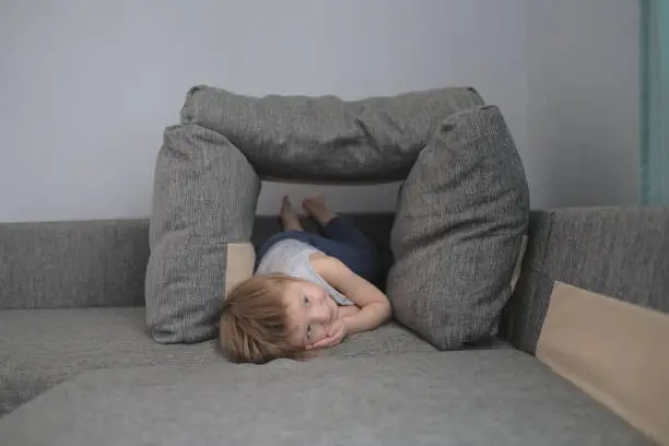 Photo of funny European child playing with pillows on couch