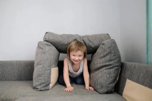 Photo of funny European child playing with pillows on couch