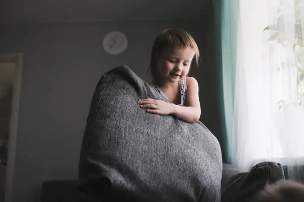 Photo of funny European child playing with pillows on couch