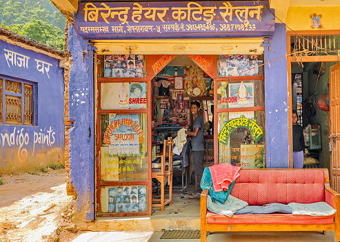 Pharping, Kathmandu valley, Nepal - April 27, 2022 : A brightly colored  barbershop in the small town of Pharping (or Phamting). The little room has no space for the waiting coach that is conveniently placed on the pavement.