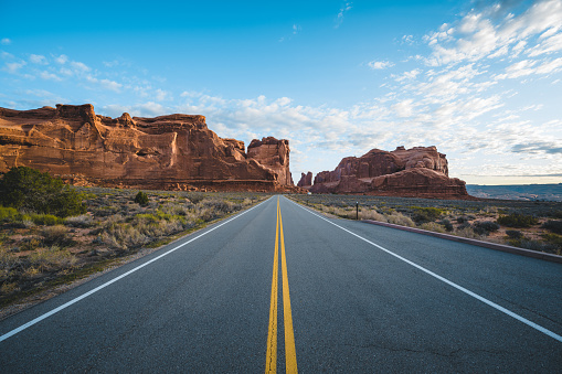 Straight desert road with yellow dividing lines seen at Arches National Park in the Southwest USA a hot summer morning.