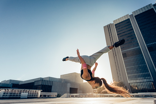 Woman doing frontflip outdoors in city. Urban sportswoman in action practicing parkour and flashkick.