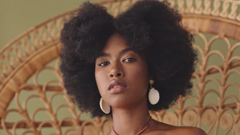 Beautiful African American woman with an afro sitting alone on a wicker chair and feeling confident. Powerful black woman with an afro feeling like a queen while posing in the studio