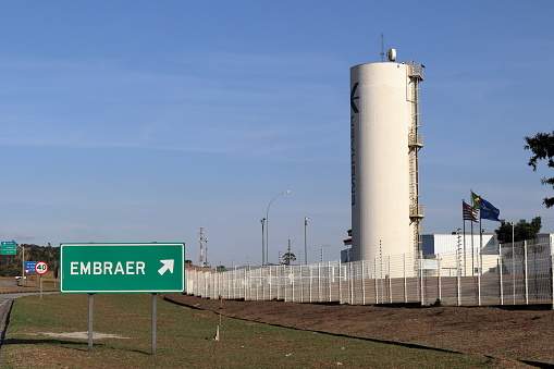 Taubate, Sao Paulo, Brazil - July 15, 2022: Board with arrow indicating Embraer in front of one of Embraer its Brazilian instalations in a sunny day. Embraer name at the company's entrance. High quality photo