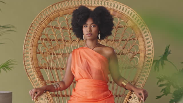 Beautiful African American woman with an afro sitting alone on a wicker chair and feeling confident. Powerful black woman with an afro feeling like a queen while posing in the studio
