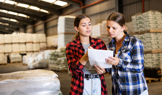 Saleswoman helping female shopper checking order list at warehouse