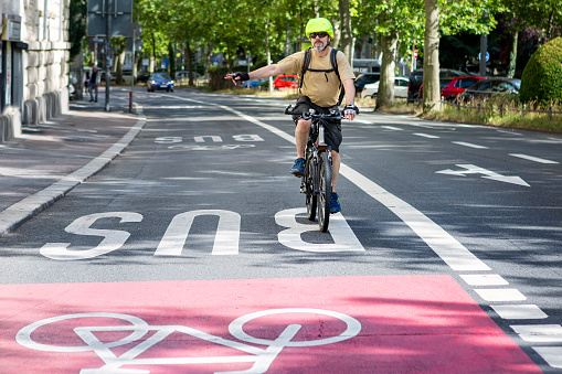 Male cyclist riding on a bike lane in the city center - giving a hand signal in order to turn right. Some unrecognisable traffic in the background.