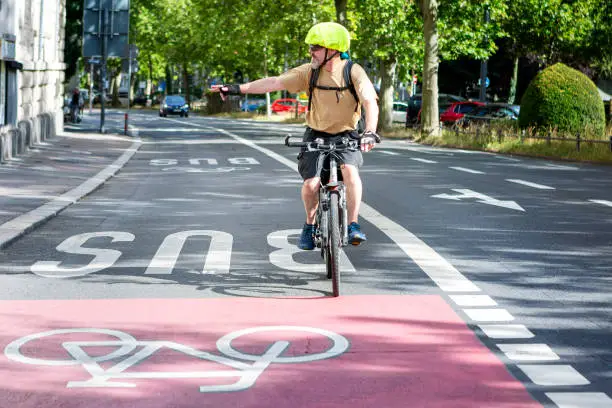 Male cyclist riding on a bike lane in the city center - giving a hand signal in order to turn right. Some unrecognisable traffic in the background.