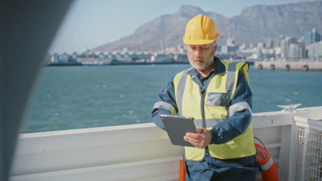 One mature marine engineer communicating with a digital tablet while working on a ship at sea. Technician and maintenance or diesel mechanic fixing repairs and mechanical issues from a ship deck