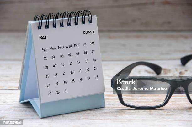 October 2023 White Desk Calendar On Wooden Table With Glasses Background Stock Photo - Download Image Now