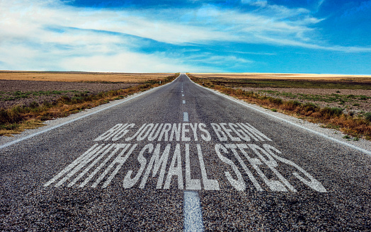 Big journeys begin with small steps written on asphalt road.