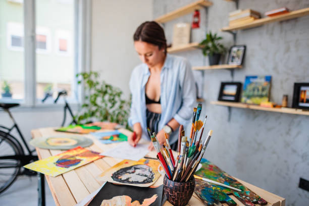istock Paintbrushes on table while female artist working in background 1408893250