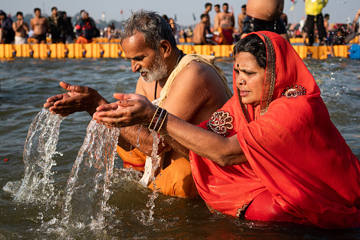 Allahabad, India - February 10, 2019: A Hindu couple praying and bathing in the sacred waters at the Triveni Sangam, the confluence of the Ganges, Yamuna and mythical Saraswati rivers, at the Kumbh Mela Festival in Allahabad (Prayagraj), Uttar Pradesh, India.