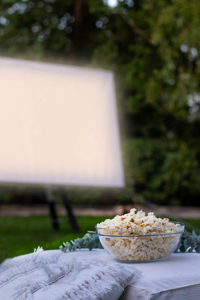 istock Vertical view of isolated popcorn bowl and a projector screen in the background playing a movie in the park at night 1408895011