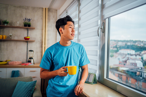 Young Asian man drinking coffee and looking through window