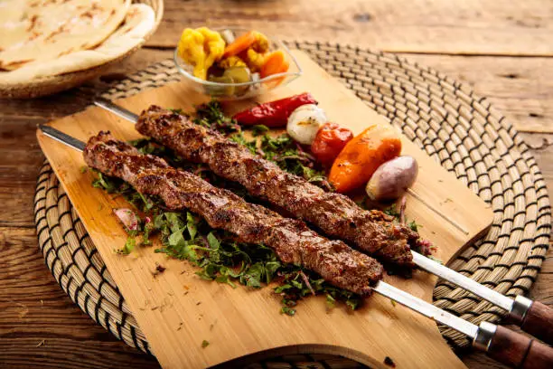 Photo of Adana Kebab served in a wooden cutting board isolated on wooden background side view