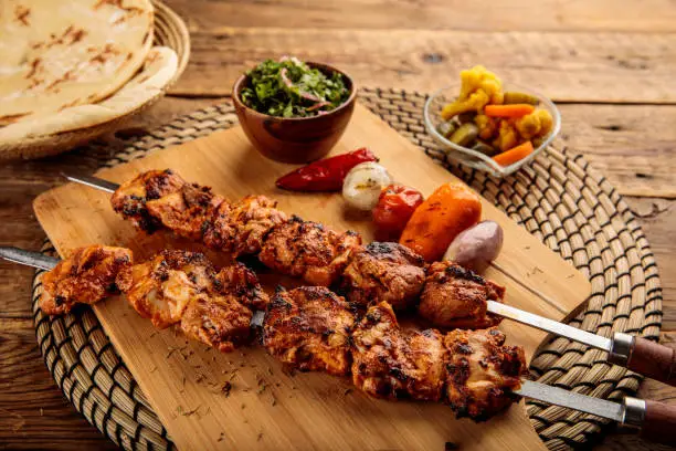 Shish Tawook kebab with pickle and bread served in a dish isolated on wooden background side view
