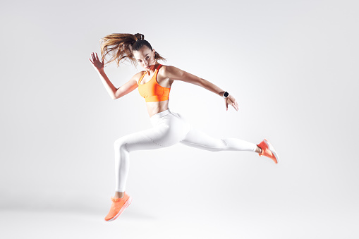 Beautiful young woman in sports clothing running against white background