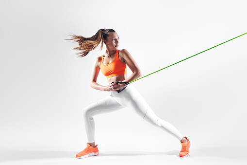 Confident young woman using resistance band while exercising against white background