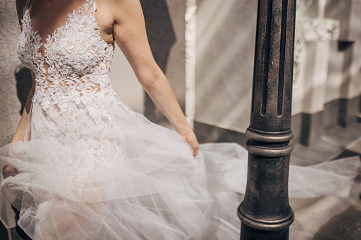 Beautiful young female is an elegant wedding dress walking on sidewalk outdoors in city.