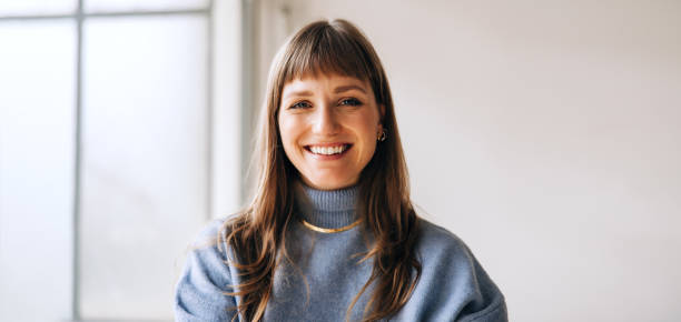 Portrait of a happy businesswoman smiling at the camera Portrait of a happy young businesswoman smiling at the camera while standing in an office. Cheerful female entrepreneur working in a creative workplace. headshot stock pictures, royalty-free photos & images