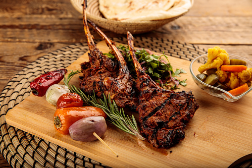 Lamb Chops with pickle and bread served in a wooden cutting board isolated on wooden background side view