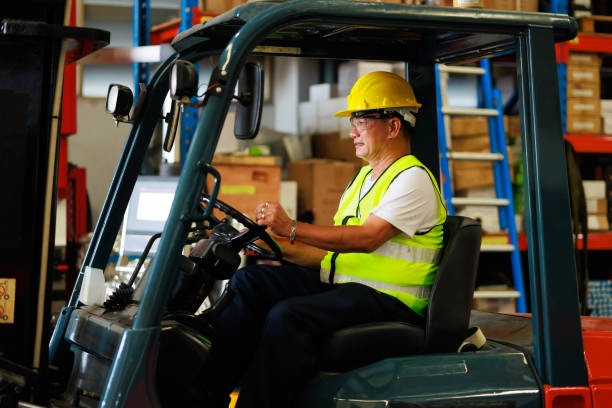 istock Warehouse staff driving forklift operator moving boxes in industrial container warehouse factory. Asian senior Man worker woking with forklift. 1408908597