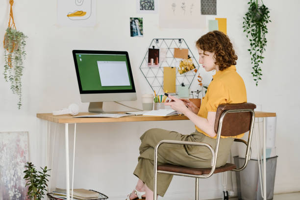 istock Young serious businesswoman scrolling in mobile phone in front of computer 1408908692