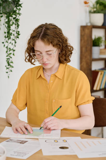Young serious freelance specialist drawing working schemes on paper