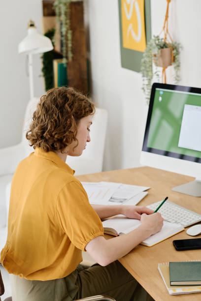 istock Young businesswoman making notes in notebook while sitting in front of computer 1408908698