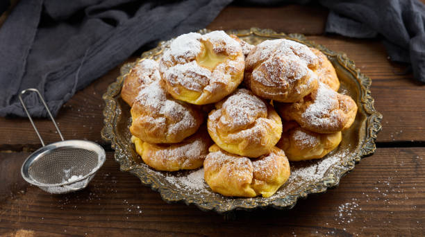 istock Baked eclairs with custard cream on a metal round plate sprinkled with powdered sugar 1408908752