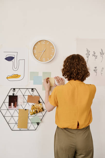 istock Back view of young creative female freelancer sticking notepapers on wall 1408908785