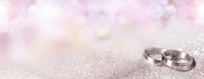 Silver wedding rings on pastel pink bokeh background. Horizontal close-up for a wedding card with space for text.