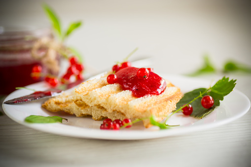 fried bread croutons for breakfast with redcurrant jam in a plate with berries on a wooden table.
