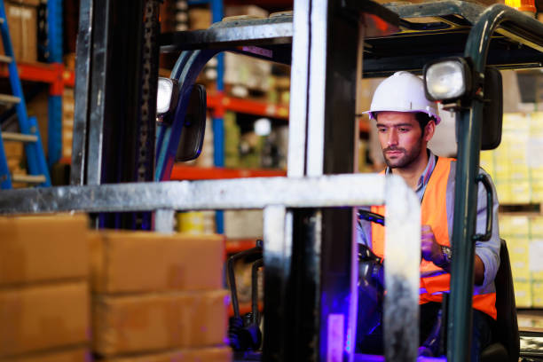 istock Warehouse staff driving forklift operator moving boxes in industrial container warehouse factory. Man worker woking with forklift. 1408913019