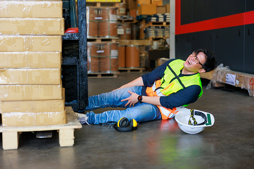 First Aid and safety first concept. Warehouse man worker lying down on floor after accident in warehouse factory. Professional engineering teamwork. Health insurance emergency accident in workplace.