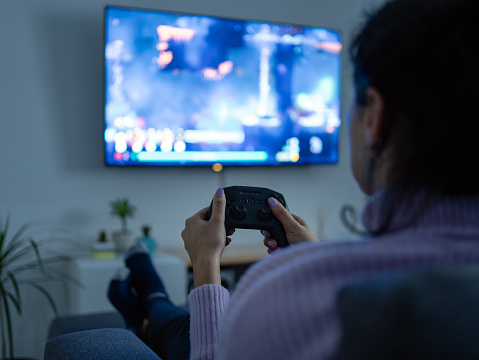 Woman playing video games with a wireless joystick in the tv room. Selective focus