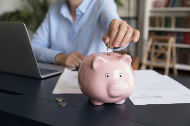 Mature business woman inserting cash into piggy bank stock photo