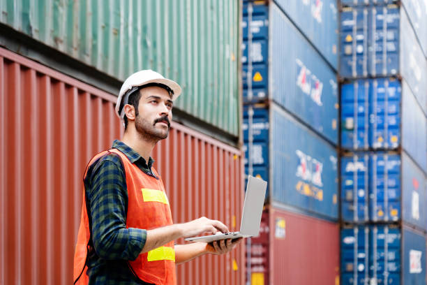 Container workers use laptops to work in port warehouses. Wear a hardhat to be safe at work. stock photo