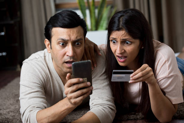 Shocked couple looking worried while using mobile phone and credit card at home