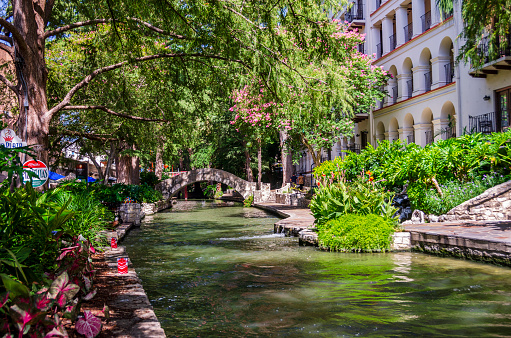 San Antonio, Texas, USA - July 2, 2018: A bridge that spans the San Antonio River which runs through the city of San Antonio, Texas. It is part of a walkway that passes many restaurants and shops that line, what is called The Riverwalk, which is a popular tourist attraction.