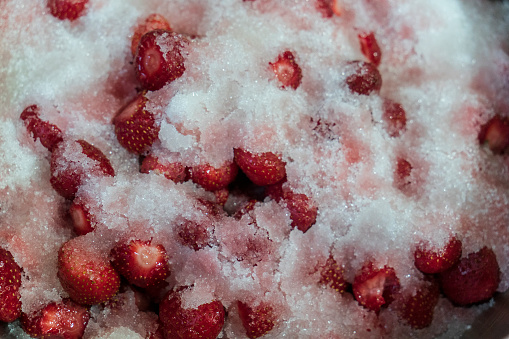 Strawberry jam making, adding sugar into the bowl with berries. Shallow depth of field.