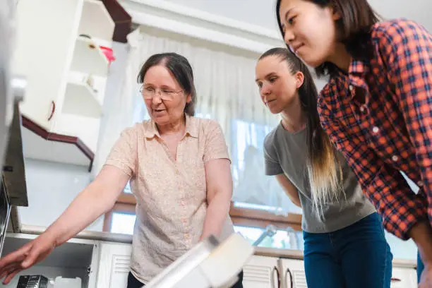 Photo of Host-mother welcoming and explaining how to use the kitchen to two multi-ethnic female tourists