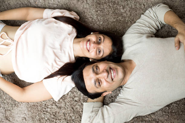 happy couple lying down on carpet at home - couple loving lying on back carpet imagens e fotografias de stock