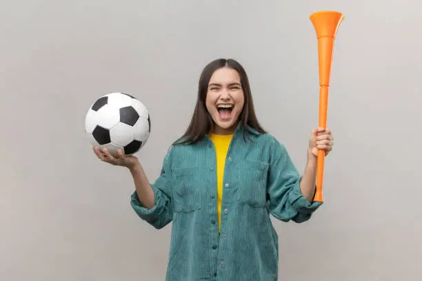 Photo of Woman holding bullhorn and soccer ball, screaming happily, supporting favorite football team.