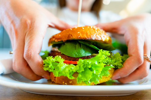 Hamburger vegan healthy vegetarian burger. Salad, avocado, vegetable on veggie sandwich eating cute woman. Tasty vegetarian healthy green food